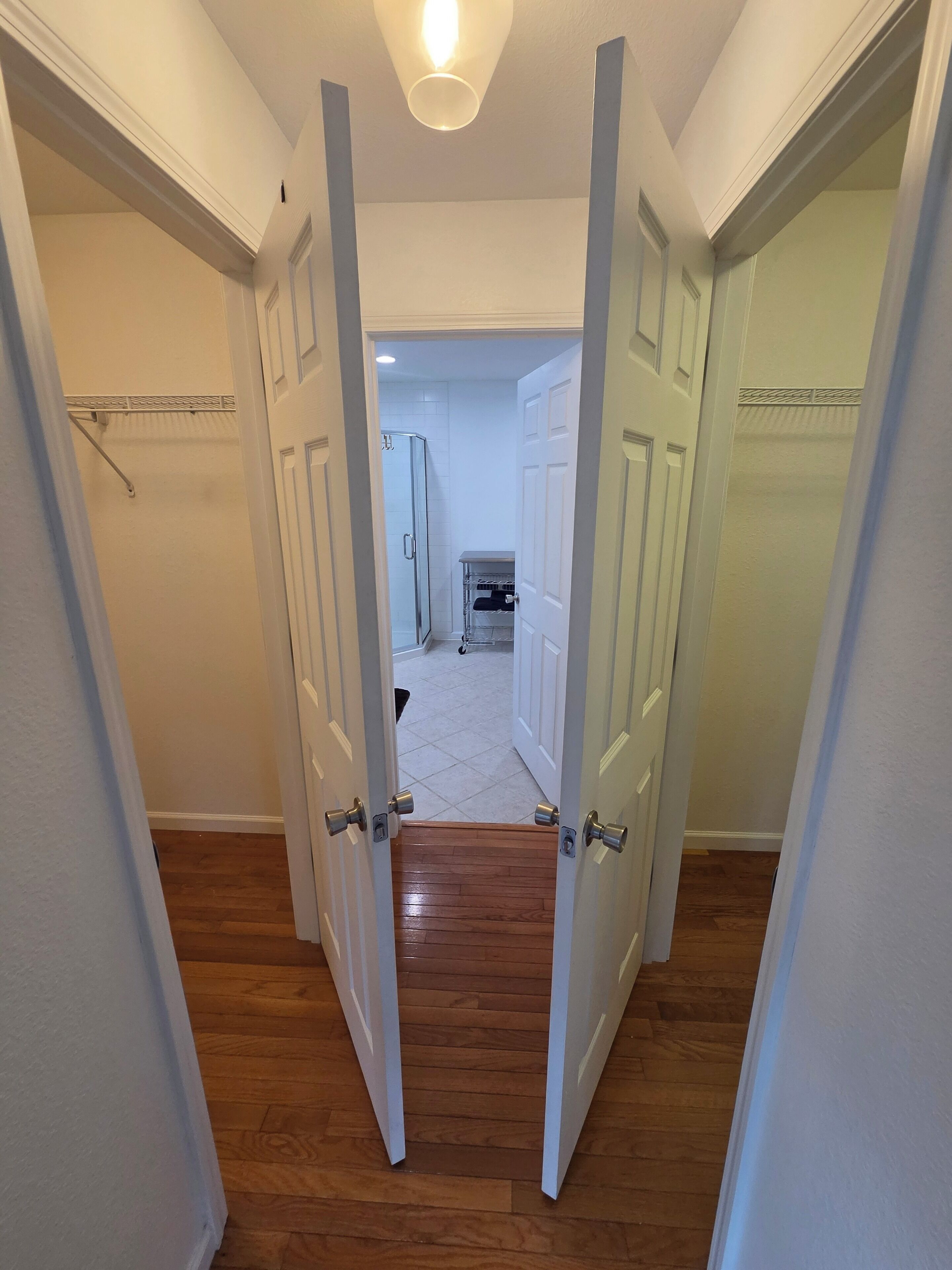 A hallway with wooden flooring leading to a closet area with open doors.