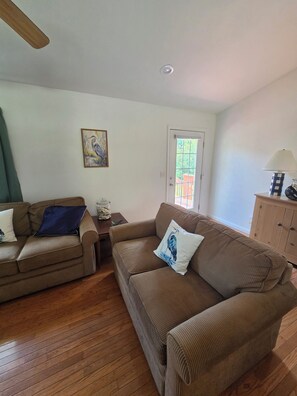 A living room with two brown sofas, a wooden floor, a painting on the wall, a door with a view, and a lamp on a side table. - Blue heron INN 3-bedroom home 2.2miles from FLW! (Saint Robert)