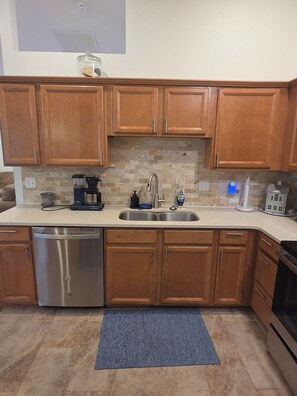 A kitchen with wooden cabinets, a stainless steel dishwasher, a double sink, and a coffee maker. - Blue heron INN 3-bedroom home 2.2miles from FLW! (Saint Robert)