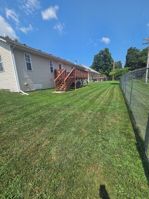 A residential property with a well-maintained lawn, a wooden deck, and a chain-link fence.