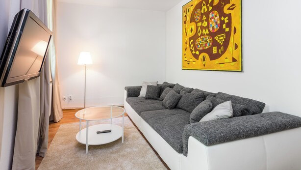 A modern living room with a sofa, a flat-screen TV, a lamp, and a large abstract painting on the wall.