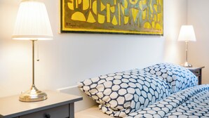 A neatly arranged bedroom with a bed, two bedside tables, and a wall-mounted abstract painting.