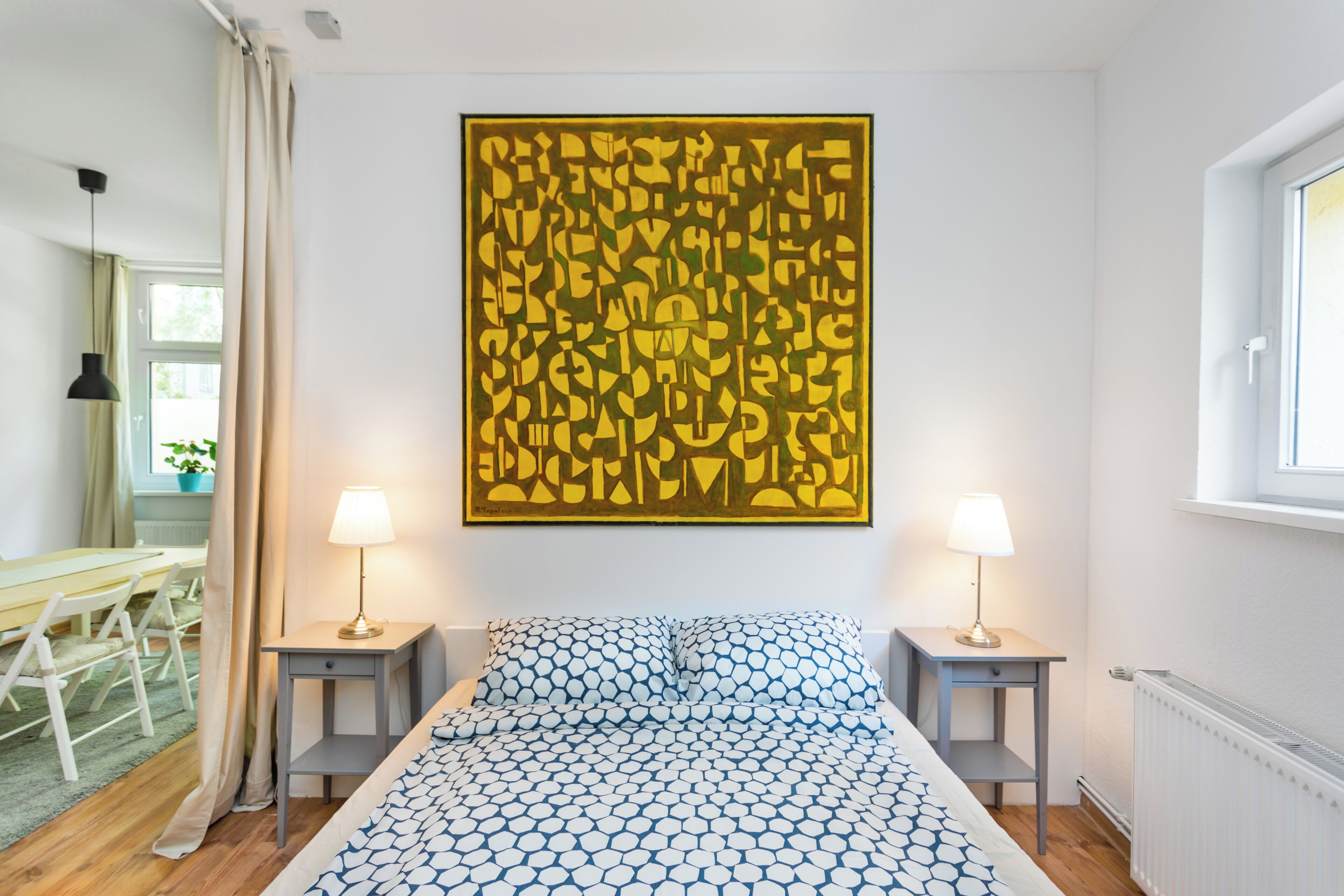 Ein Schlafzimmer mit einem Bett, zwei Nachttischen mit Lampen, einem großen abstrakten Gemälde an der Wand und einem Fenster.