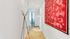 A hallway with a wooden floor, a painting on the right wall, and a sculpture on the left.