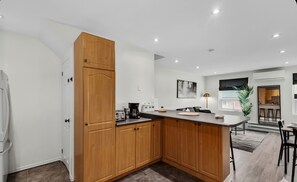 A modern kitchen with wooden cabinets, a countertop, and a dining area with a table and chairs. - 2BR Home | Free Parking | Fast WiFi (Toronto)
