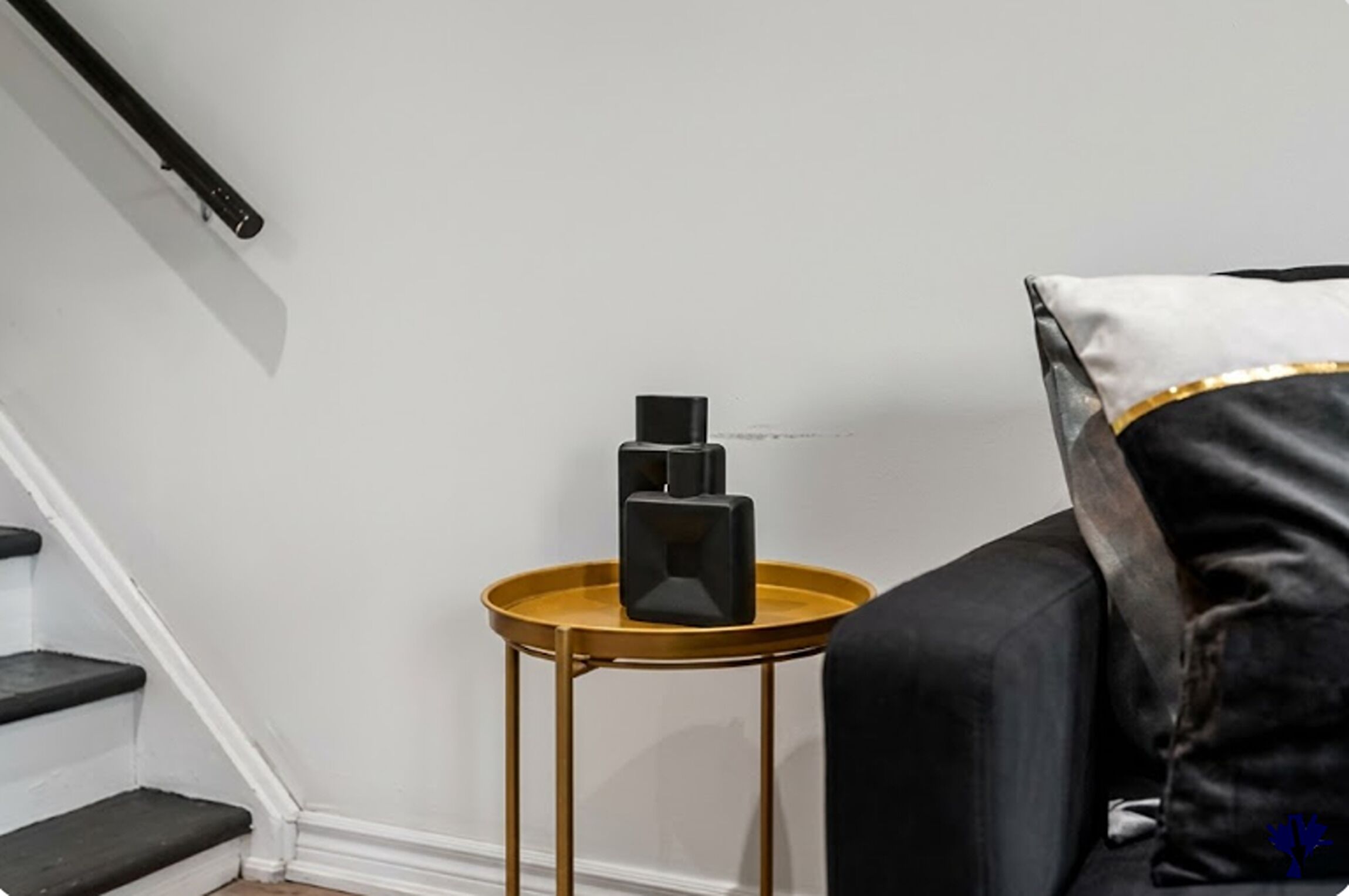 A staircase with a black handrail, a small round wooden table with a black object on it, and a black and white sofa with a blue design.