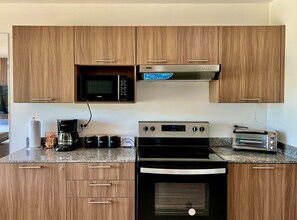 A kitchen with wooden cabinets, a microwave, a coffee maker, a toaster, and an oven. - Cozy 1-bedroom apartment with AC in fantastic San Salvador (San Salvador)