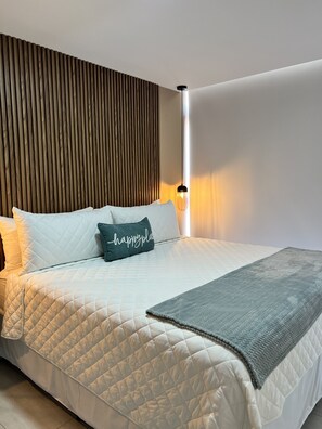 A neatly made bed with a quilted cover, a grey throw blanket, and a pillow with the text 'happy place.' - Cozy 1-bedroom apartment with AC in fantastic San Salvador (San Salvador)