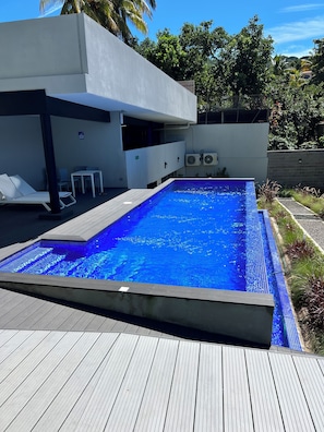 A swimming pool with a wooden deck, a lounge area with chairs, and a modern building structure. - Cozy 1-bedroom apartment with AC in fantastic San Salvador (San Salvador)