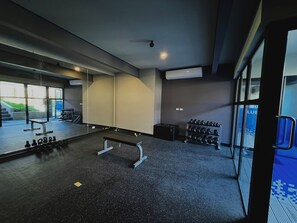 Ein Fitnessraum mit Spiegelwand, einer Bank, Hanteln und einem Laufband.