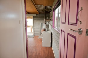 A narrow hallway with a wooden ceiling, a white refrigerator, and a window with a purple door.