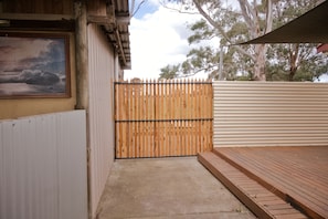 A wooden gate leading to a concrete pathway, a corrugated metal fence, and a wooden deck.