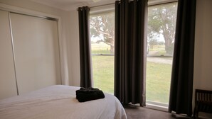 Una habitació d'hotel amb un llit, una finestra amb cortines, una cadira i vista a una zona verda.