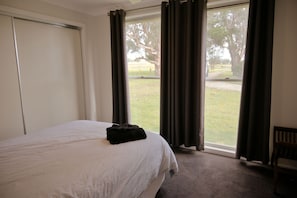 A hotel room with a bed, a window with curtains, a chair, and a view of a grassy area.