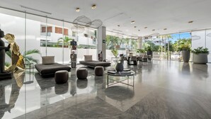 A modern hotel lobby with a glass wall, a seating area with sofas and ottomans, a coffee table, and a dining area. - Luxury in Marina Vallarta Gym Roof Pool (Puerto Vallarta)