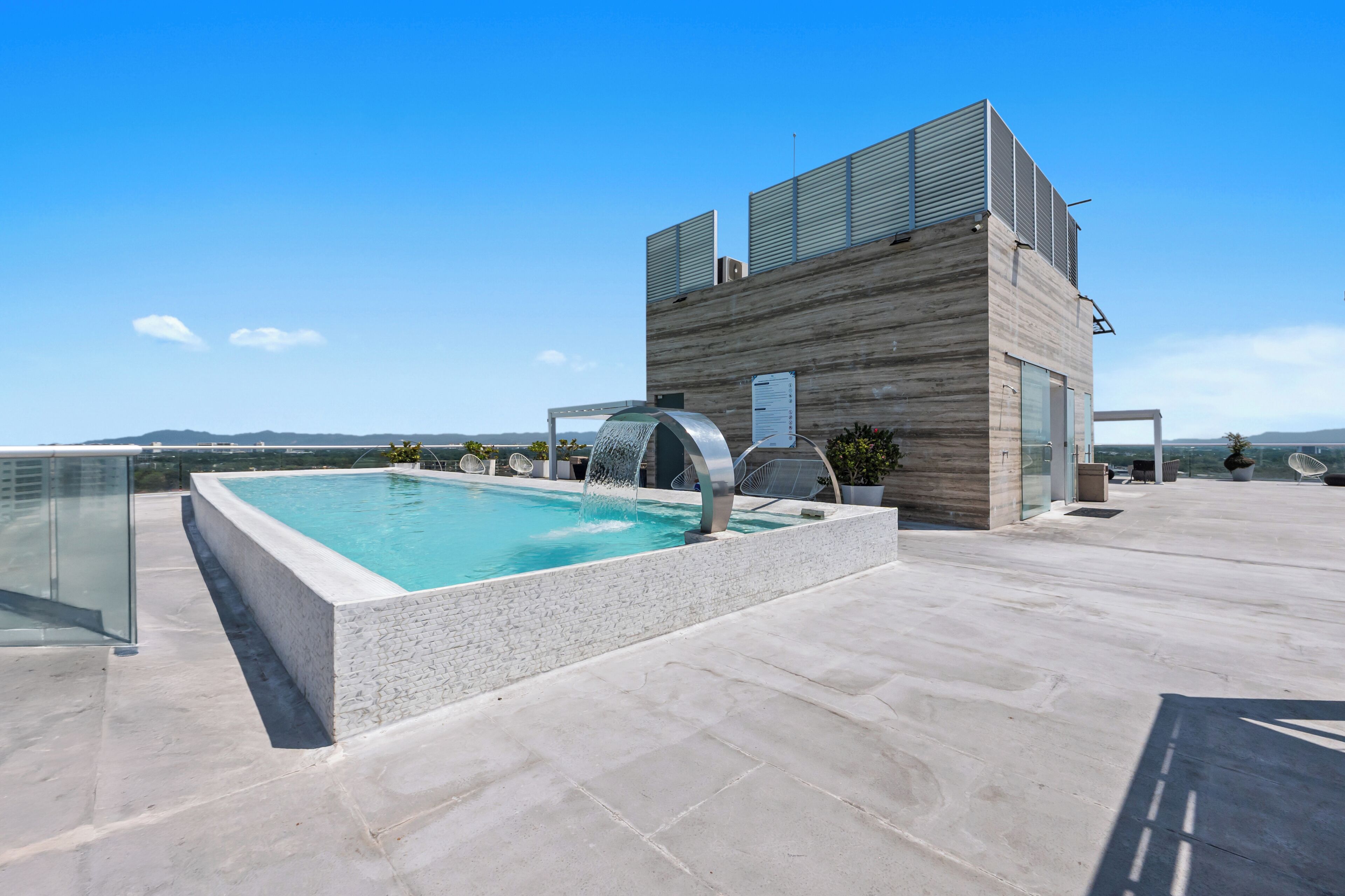 Une piscine sur le toit, avec un bâtiment moderne en arrière-plan, un ciel dégagé et un paysage lointain.