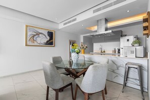 A modern kitchen with a glass dining table, grey upholstered chairs, and a marble backsplash. - Luxury in Marina Vallarta Gym Roof Pool (Puerto Vallarta)