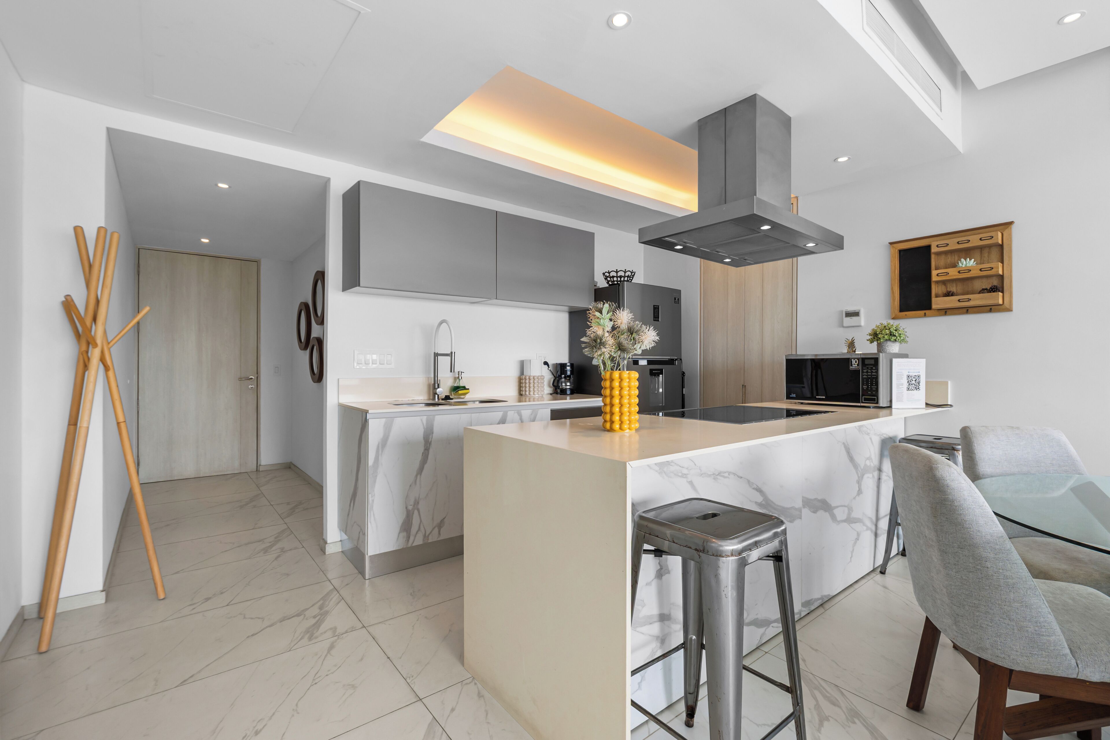 Una cocina moderna con una isla central, taburetes de bar y una zona de comedor con mesa de vidrio.
