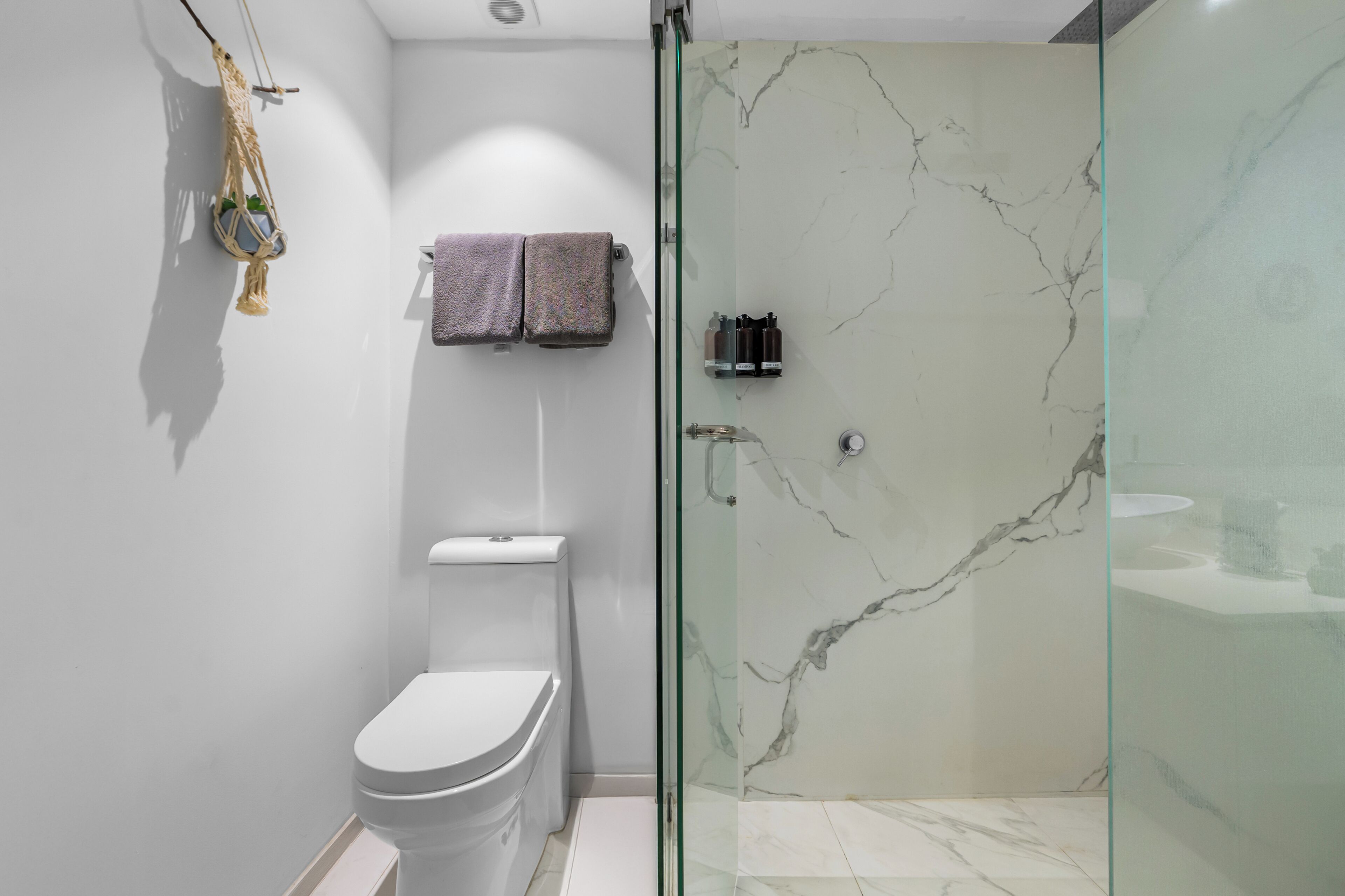 Un baño moderno con inodoro, ducha con mampara de vidrio y paredes de mármol.
