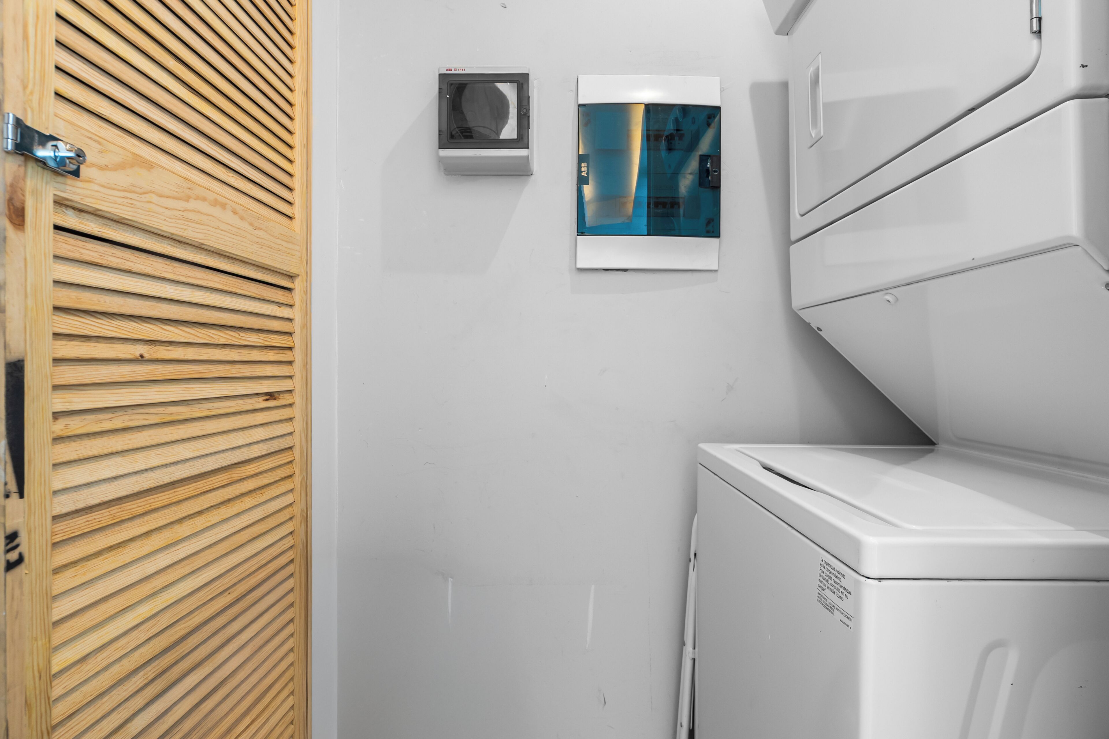 Une buanderie avec une porte à lattes en bois, un lave-linge blanc et un sèche-linge fixé au mur.