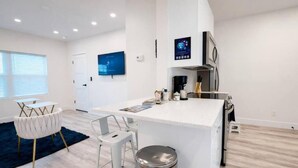 A modern kitchen with a white countertop, stainless steel appliances, and a small dining area with white chairs. - Wavecrest Retreat On Strip  (Daytona Beach)