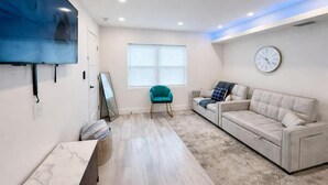 A modern living room with a flat-screen TV, a sofa, a teal armchair, and a large window. - Wavecrest Retreat On Strip  (Daytona Beach)
