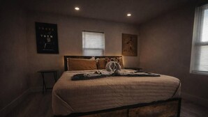 A bedroom with a large bed, a bedside table, a window with blinds, and a poster on the wall. - Wavecrest Retreat On Strip  (Daytona Beach)