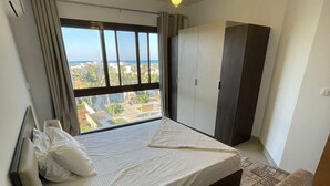 A bedroom with a bed, a wardrobe, a window with a view, and a patterned rug. - 
    Marassi Marina 1 Sea View (Marsa Matrouh)