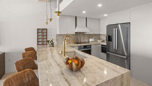 A modern kitchen with a marble countertop, stainless steel appliances, wicker chairs, and pendant lighting. - Bay Pearl - Bradenton Beach Condo by Anna Maria Life Vacation Rentals (Bradenton Beach)
