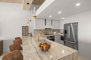Una cocina moderna con encimera de mármol, electrodomésticos de acero inoxidable, sillas de mimbre e iluminación colgante.