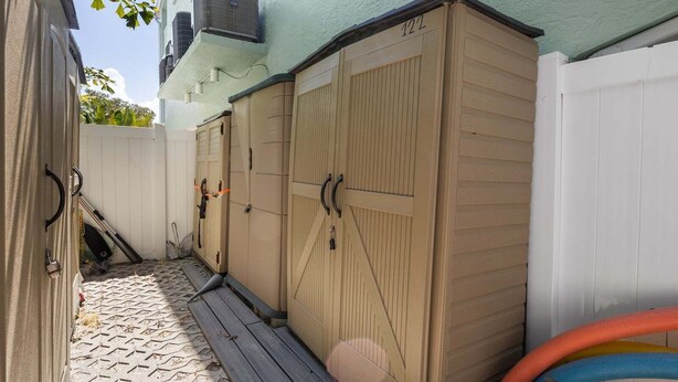 A covered outdoor area with storage cabinets, a white fence, and a paved walkway. - Bay Pearl - Bradenton Beach Condo by Anna Maria Life Vacation Rentals (Bradenton Beach)