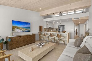 Una sala moderna con un mostrador de recepción de madera, un televisor de pantalla plana grande, un sofá y una zona de cocina con taburetes de bar.