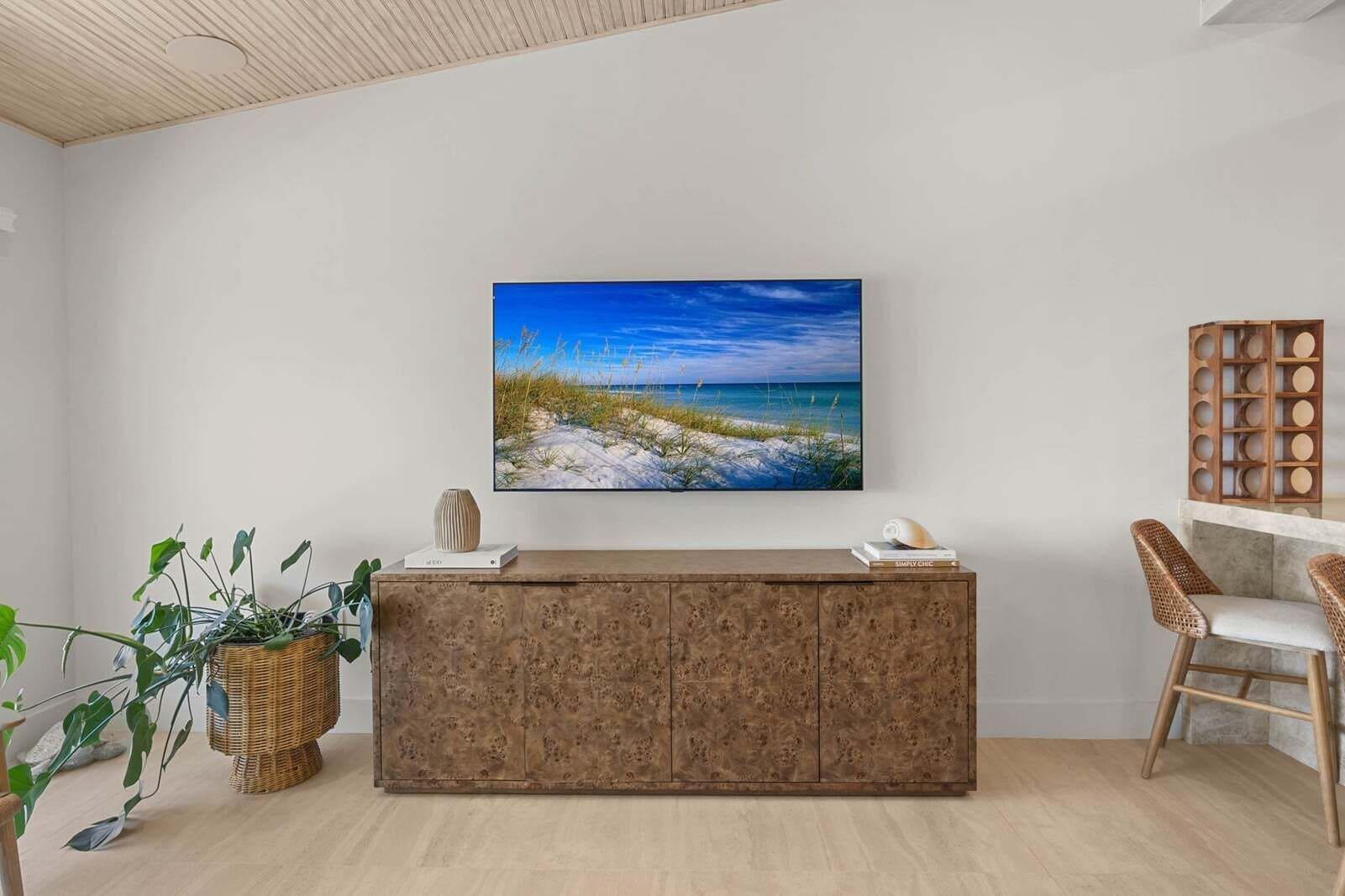 Una habitación con un armario de madera, un televisor montado en la pared, muebles de mimbre y una planta.