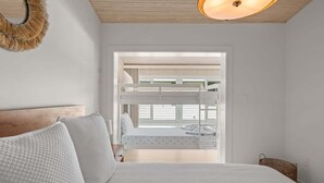 A bedroom with bunk beds, a bed with pillows, a hanging light fixture, and a window with blinds. - Bay Pearl - Bradenton Beach Condo by Anna Maria Life Vacation Rentals (Bradenton Beach)