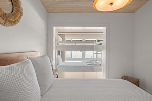 Un dormitorio con literas, una cama con almohadas, una lámpara colgante y un ventanal con persianas.