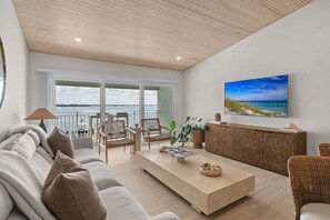 Ein modernes Wohnzimmer mit einer Couch, Sesseln, einem Couchtisch und einem Fernseher an der Wand.