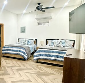 A bedroom with two beds, a ceiling fan, an air conditioning unit, and a TV. - Depa Azul+Green Spot, Entire Duplex, 4BR-Sleeps 12 (Puerto Peñasco)