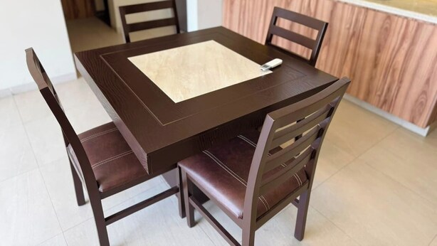 Une table à manger avec quatre chaises, un coin cuisine comprenant un évier et un plan de travail, et un sol carrelé.