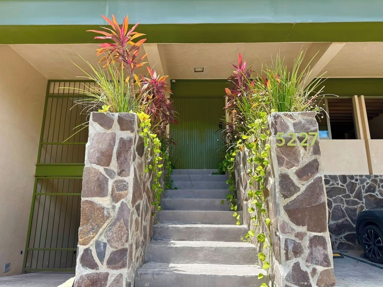 Uma escadaria com pilares de pedra, levando a uma porta com um portão verde.