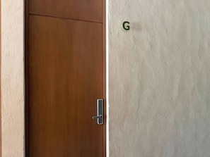Uma porta de madeira com puxador moderno, parede texturizada com a letra 'G' visível, e parte de uma parede bege.