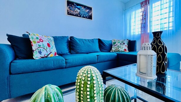 Ein modernes Wohnzimmer mit einem blauen Sofa, dekorativen Kissen, einem Glastisch und einer Sukkulentenskulptur.