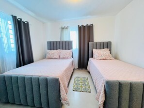 Een slaapkamer met twee eenpersoonsbedden, een kamerkleed met patroon en gordijnen.