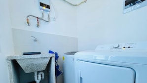 Ein Waschraum mit Waschmaschine, Spüle und Warmwasserbereiter.