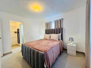 A bedroom with a bed, nightstand, and a door leading to a bathroom. - 2-bedroom  spacious apartment in tranquil Punta Cana, very close to the mall (Punta Cana)