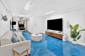 Ein modernes Wohnzimmer mit blauem Boden, einem großen Flachbildfernseher, einem weißen Sofa, einem Couchtisch und einer Topfpflanze.