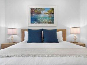 A neatly arranged hotel room with a bed, two bedside lamps, a framed painting, and a textured throw blanket.