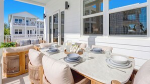 A dining area with a table set for four, surrounded by wicker chairs, and a view of a white building with balconies. - The Lighthouse | Ocean and Pool Views, Game Room, Pool + Dock Access (Islamorada)