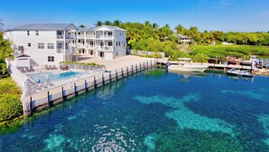 A large white building with multiple balconies, a swimming pool, and a dock with boats. - The Lighthouse | Ocean and Pool Views, Game Room, Pool + Dock Access (Islamorada)