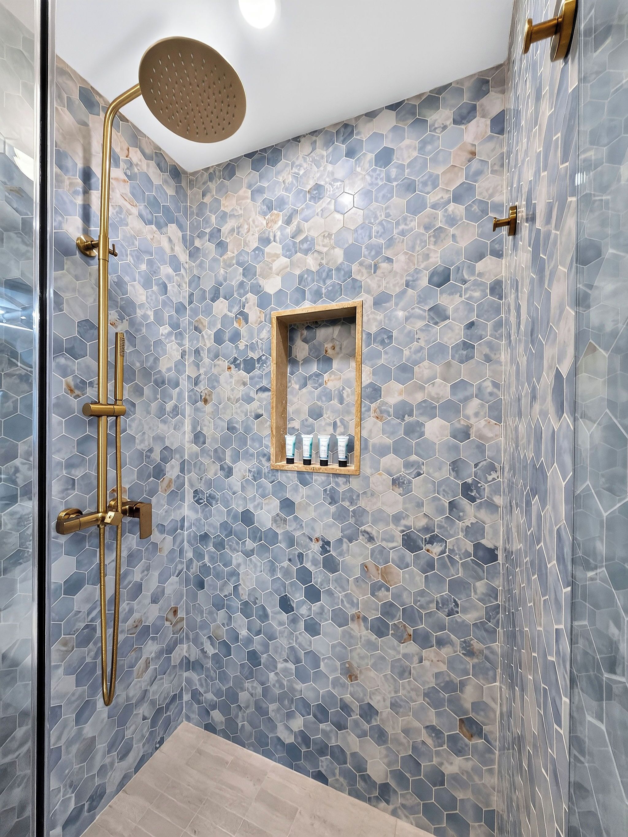 A shower with a gold showerhead and a glass door.