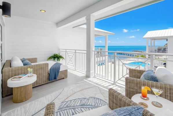 A balcony with a view of the ocean, wicker furniture, a white sofa, and a small table with drinks.